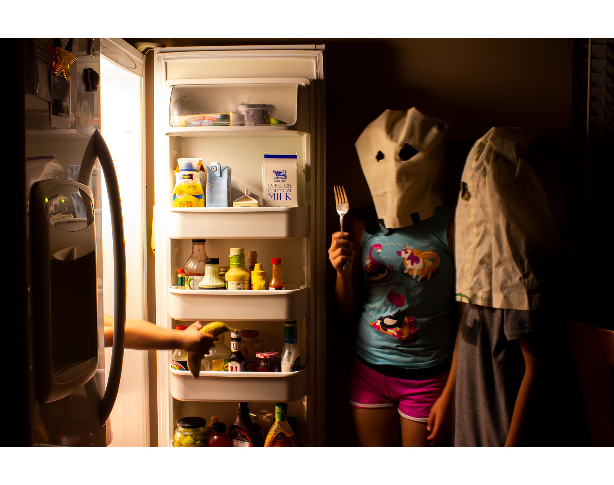 two children looking into a refrigerator dressed as ghosts