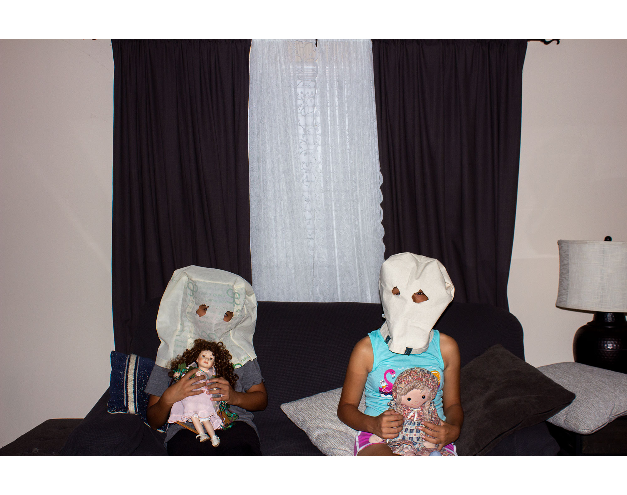 two children sitting on a couch dressed as ghosts holding dolls